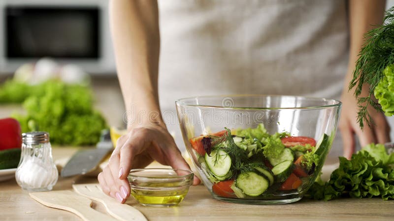 Esposa joven que sostiene el aceite de oliva que viste el cuenco para sazonar la ensalada fresca, adietando fotografía de archivo Esposa joven que sostiene el aceite de oliva que viste el cuenco para sazonar la ensalada fresca, adietando fotografía de archivo