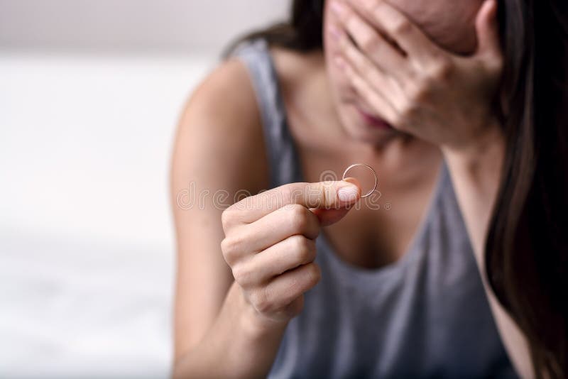 Esposa trastornada que está de luto después del divorcio que lleva a cabo un anillo de bodas que se sienta en un sofá blanco imagen de archivo libre de regalías Esposa trastornada que está de luto después del divorcio que lleva a cabo un anillo de bodas que se sienta en un sofá blanco imagen de archivo libre de regalías