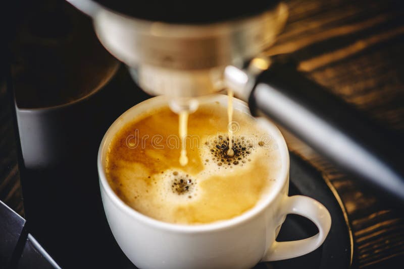 Espresso pours from the coffee machine into a white Cup forming golden foam