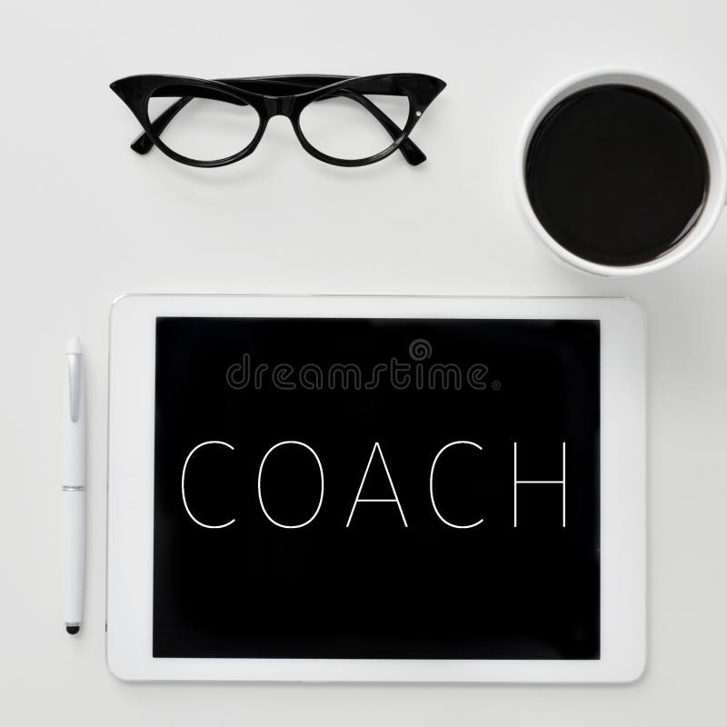 High-angle shot of a desk with a tablet computer with the word coach written in it, a pair of women eyeglasses and a cup of coffee. High-angle shot of a desk with a tablet computer with the word coach written in it, a pair of women eyeglasses and a cup of coffee