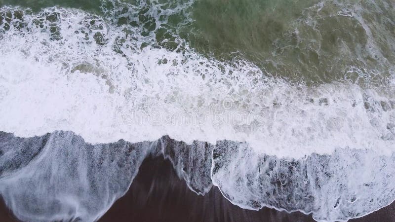 Espumando o mar ou as ondas do oceano rolam na praia arenosa durante o tiroteio de drones