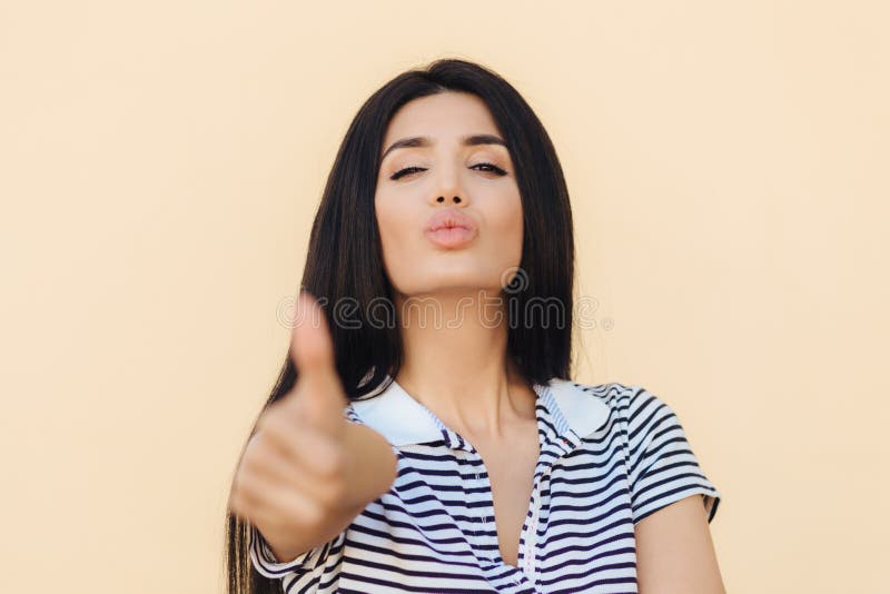 Essa multa do ` s! A fêmea saudável bonita com cabelo escuro, olhares seguramente na câmera, polegar dos aumentos como mostra com imagens de stock royalty free Essa multa do ` s! A fêmea saudável bonita com cabelo escuro, olhares seguramente na câmera, polegar dos aumentos como mostra com imagens de stock royalty free