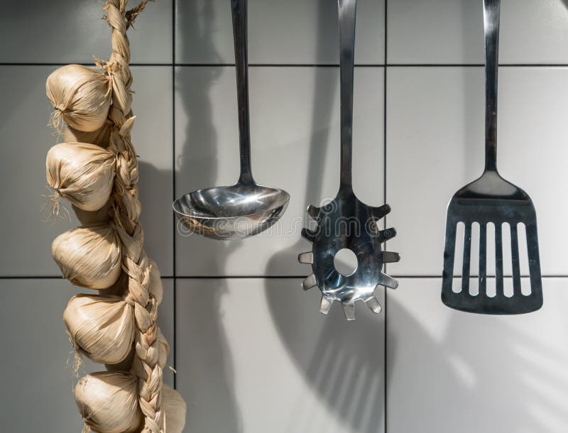 Essential kitchen utensils and decorative artificial garlic chain hanging on hook of metal rail