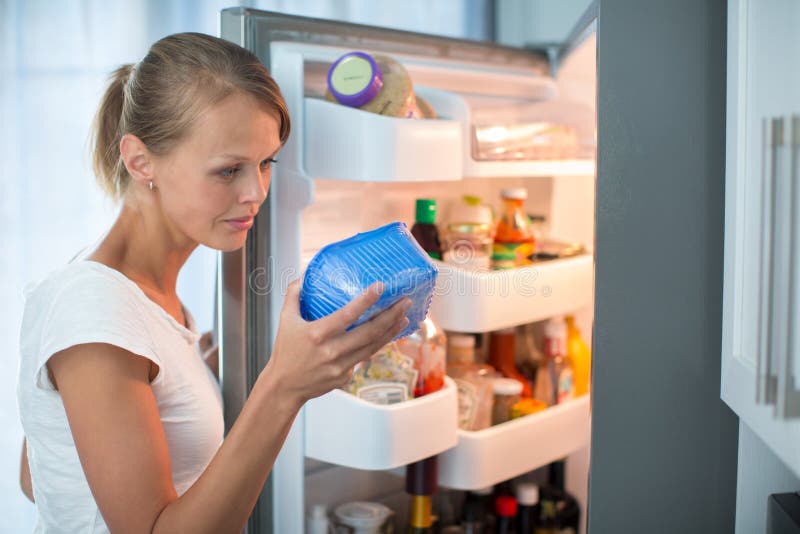 Is this still fine? Pretty, young woman in her kitchen by the fridge, looking at the expiry date of a product she took from her fridge -. Is this still fine? Pretty, young woman in her kitchen by the fridge, looking at the expiry date of a product she took from her fridge -