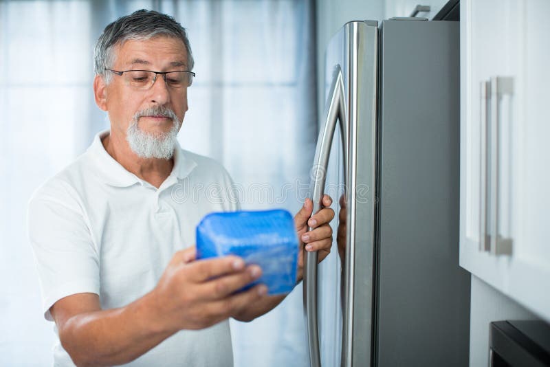 Is this still fine? Senior man in his kitchen by the fridge, looking at the expiry date of a product she took from her fridge -. Is this still fine? Senior man in his kitchen by the fridge, looking at the expiry date of a product she took from her fridge -