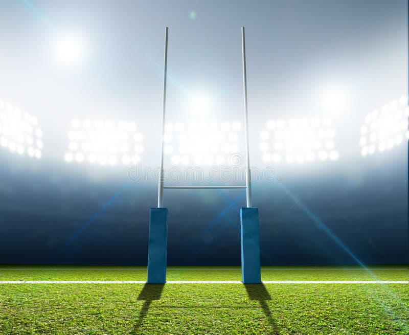 A rugby stadium with rugby posts on a marked green grass pitch at night under illuminated floodlights. A rugby stadium with rugby posts on a marked green grass pitch at night under illuminated floodlights