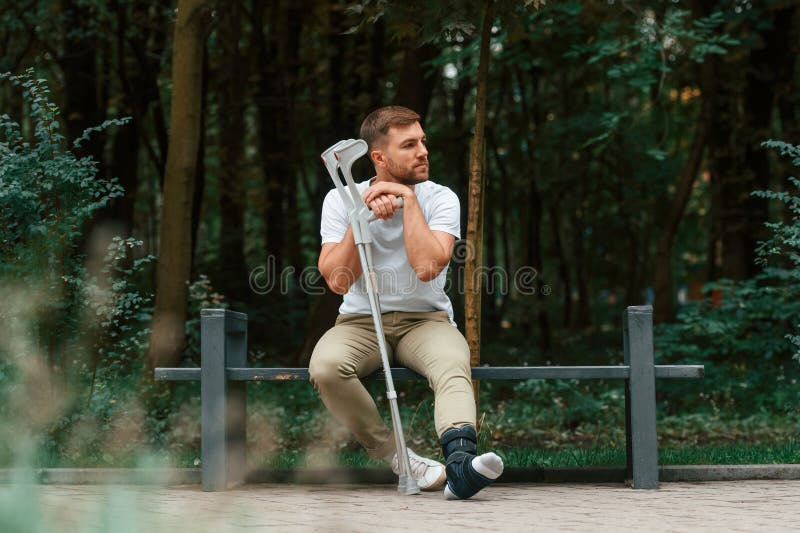 Estar aburrido y triste. hombre con muletas está en el parque al aire libre. lesión en la pierna imagen de archivo