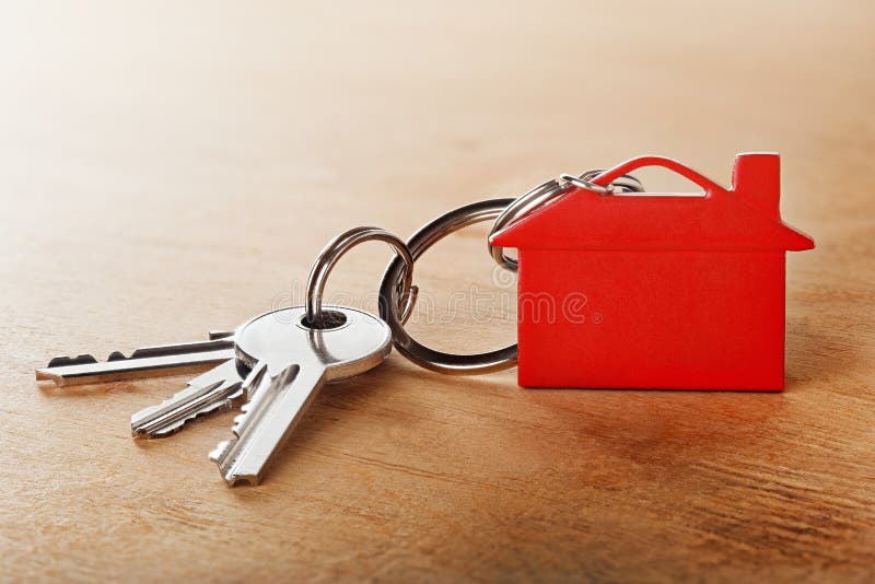 Estate concept with key, red keychain, house symbol wooden background