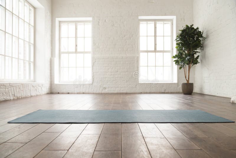 Estera desenrollada de la yoga en piso de madera en estudio de la yoga