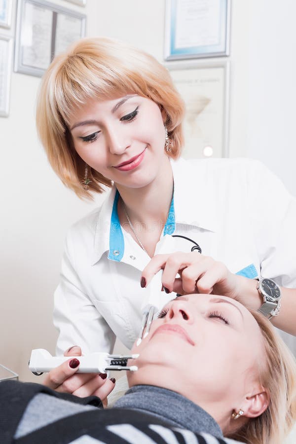 Estetista permanente della bella giovane donna bionda in un abito bianco fotografia stock Estetista permanente della bella giovane donna bionda in un abito bianco fotografia stock