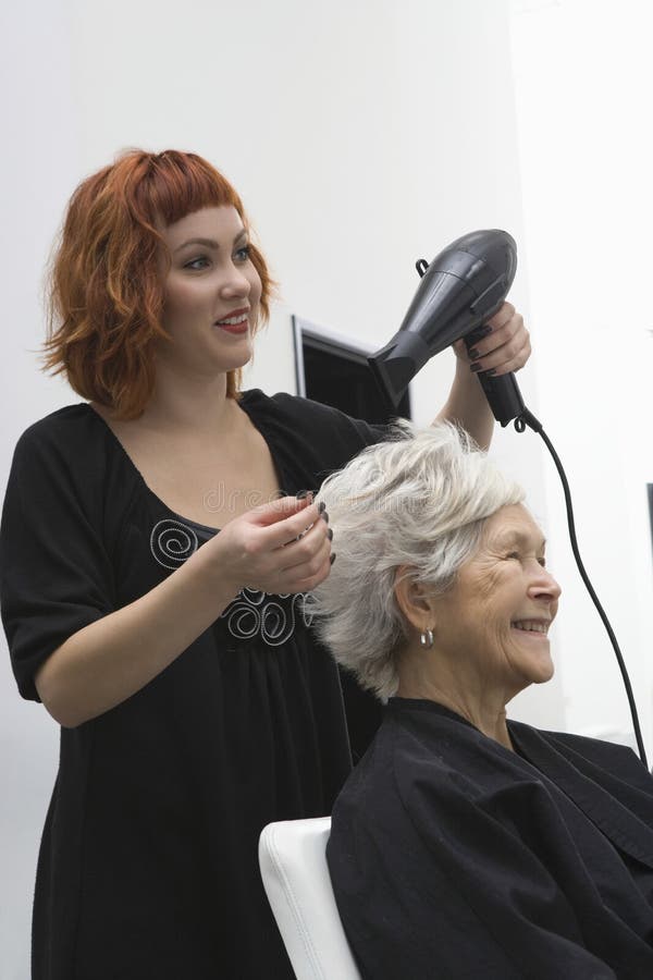 Estilista que hace el brushing el pelo de la mujer mayor