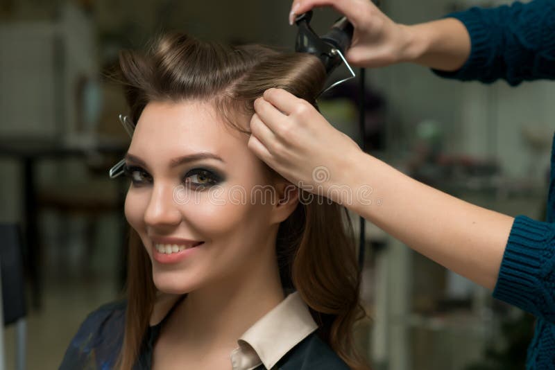 Estilista que hace rizos a la mujer morena Trabajo del peluquero imagen de archivo Estilista que hace rizos a la mujer morena Trabajo del peluquero imagen de archivo