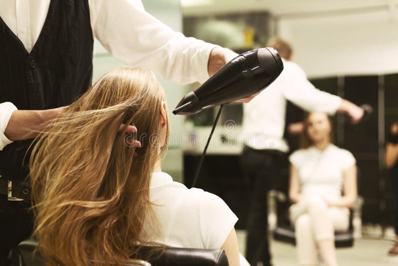 Cabeleireiro seca o cabelo com uma mulher de secador de cabelo no