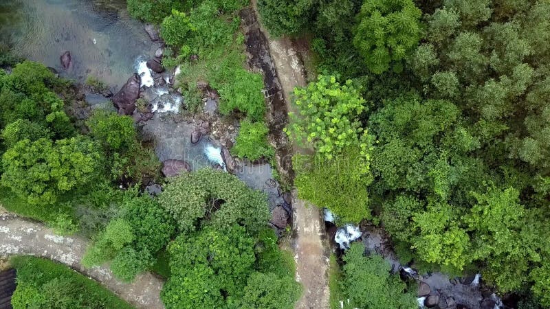 Estrada à terra da vista aérea que meandra ao longo do rio com cascatas