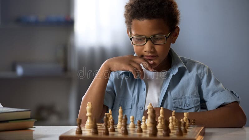Senta-se à mesa e joga xadrez a criança concentra-se no jogo