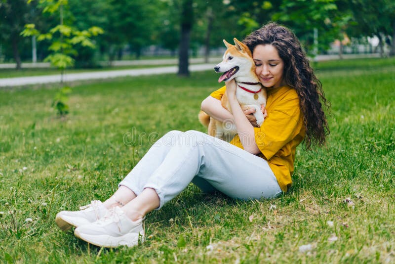 Estudante bonita que abraça o cachorrinho do inu do shiba no gramado verde no parque foto de stock Estudante bonita que abraça o cachorrinho do inu do shiba no gramado verde no parque foto de stock