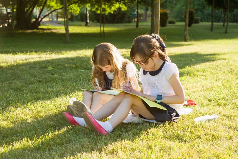 A estudante de dois amigos de menina aprende o assento em um prado no parque Crianças com trouxas, livros, cadernos Vista do th fotos de stock royalty free A estudante de dois amigos de menina aprende o assento em um prado no parque Crianças com trouxas, livros, cadernos Vista do th fotos de stock royalty free