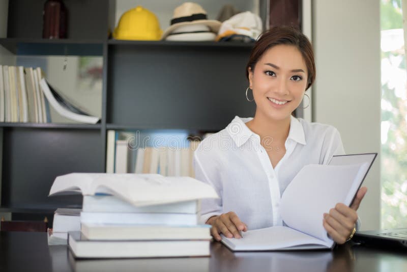 Estudante de mulheres asiático que sorri e que lê um livro para o abrandamento foto de stock Estudante de mulheres asiático que sorri e que lê um livro para o abrandamento foto de stock