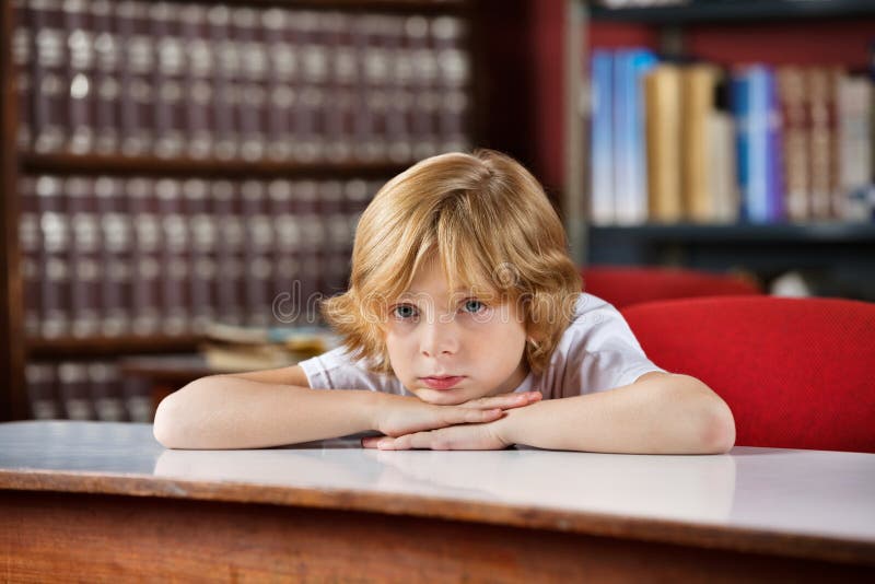 Estudante furada que inclina-se na tabela na biblioteca foto de stock royalty free Estudante furada que inclina-se na tabela na biblioteca foto de stock royalty free