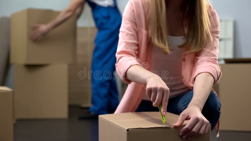 Estudante fêmea que desembala coisas na sala, bagagem levando do trabalhador da empresa de mudanças imagem de stock royalty free Estudante fêmea que desembala coisas na sala, bagagem levando do trabalhador da empresa de mudanças imagem de stock royalty free