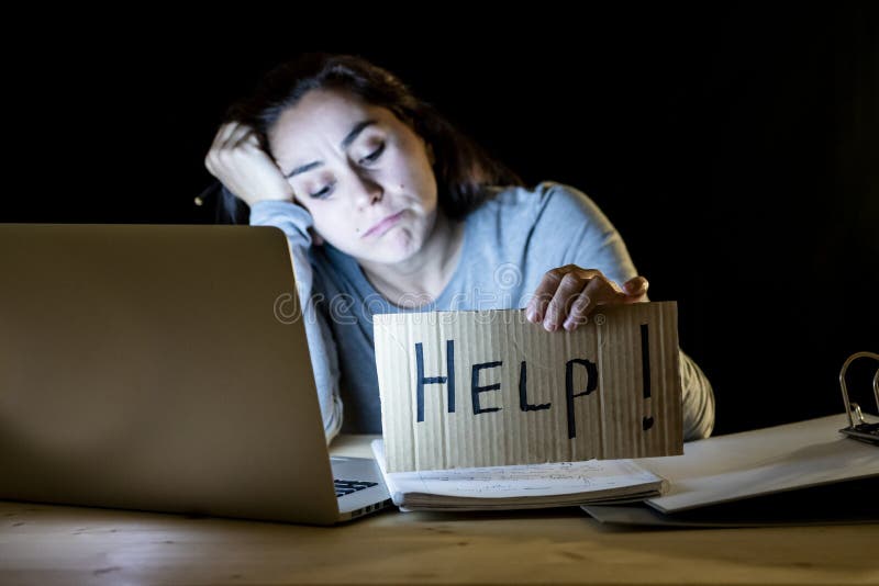 Estudante novo que trabalha tarde na noite em seu computador que guarda um sinal da ajuda foto de stock royalty free Estudante novo que trabalha tarde na noite em seu computador que guarda um sinal da ajuda foto de stock royalty free
