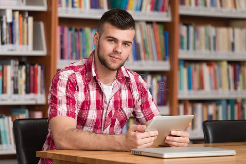 Estudante novo Using His Laptop em uma biblioteca foto de stock royalty free Estudante novo Using His Laptop em uma biblioteca foto de stock royalty free