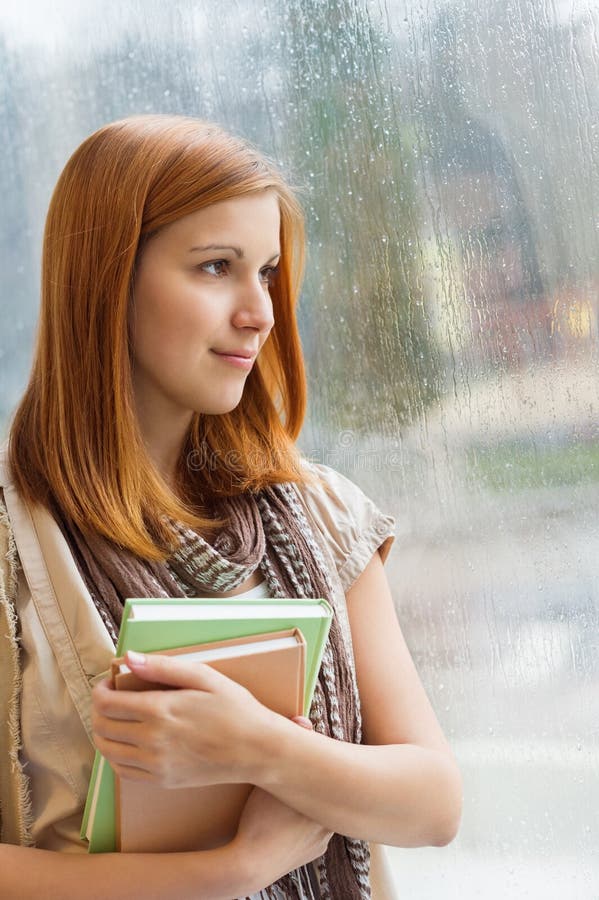 Estudante pensativo com os livros pela janela imagens de stock Estudante pensativo com os livros pela janela imagens de stock