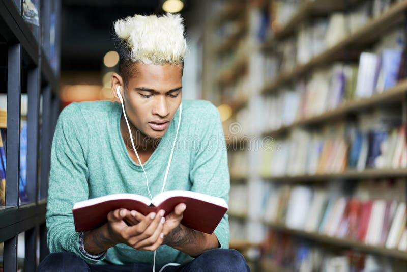 Estudante pensativo no livro de leitura dos fones de ouvido fotografia de stock Estudante pensativo no livro de leitura dos fones de ouvido fotografia de stock