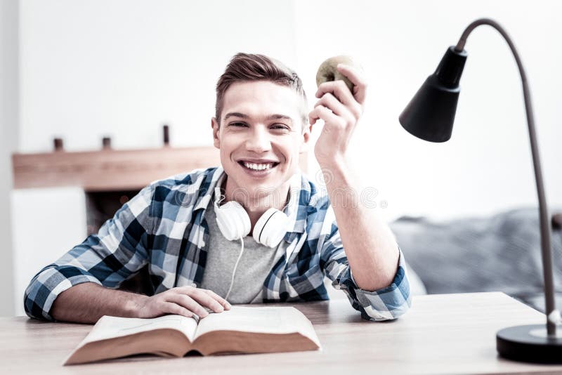 Estudante positivo que sorri ao ler e ao guardar a maçã imagens de stock royalty free Estudante positivo que sorri ao ler e ao guardar a maçã imagens de stock royalty free