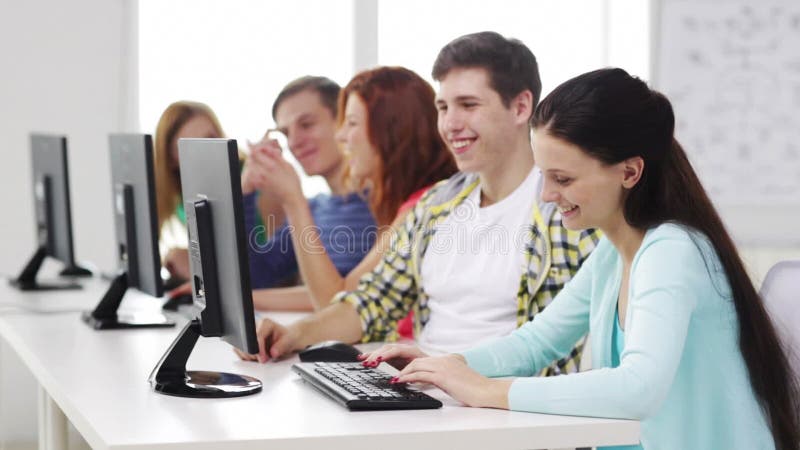 Estudantes de sorriso que trabalham com os computadores na escola