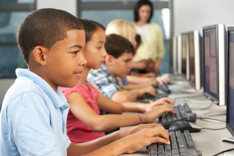 Estudantes elementares que trabalham em computadores na sala de aula