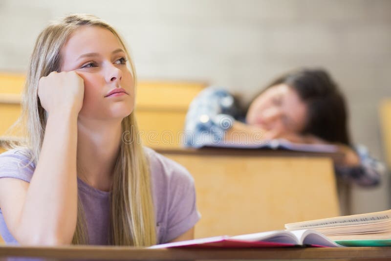 Estudiante aburrido que escucha mientras que el dormir del compañero de clase imagenes de archivo