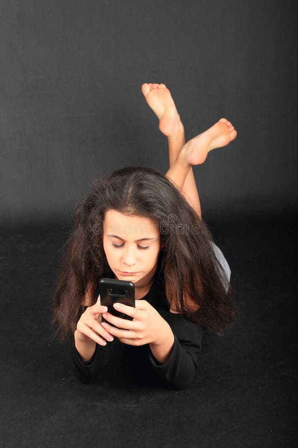 Bored teenage girl - schoolkid with brunette hair dressed in black blouse playing with smartphone or writing SMS. Communication and technology concept. Bored teenage girl - schoolkid with brunette hair dressed in black blouse playing with smartphone or writing SMS. Communication and technology concept.