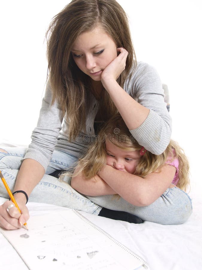 Teen student doing homework as younger sister looks on. Teen student doing homework as younger sister looks on.