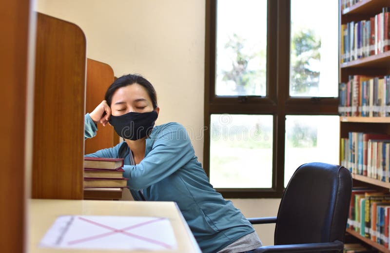 Estudiante femenina con máscara de cara durmiendo en una biblioteca universitaria foto de archivo libre de regalías