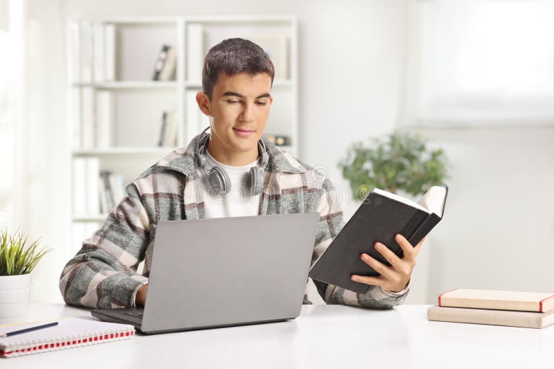 Estudiante masculino estudiando con una computadora portátil y un libro imagen de archivo