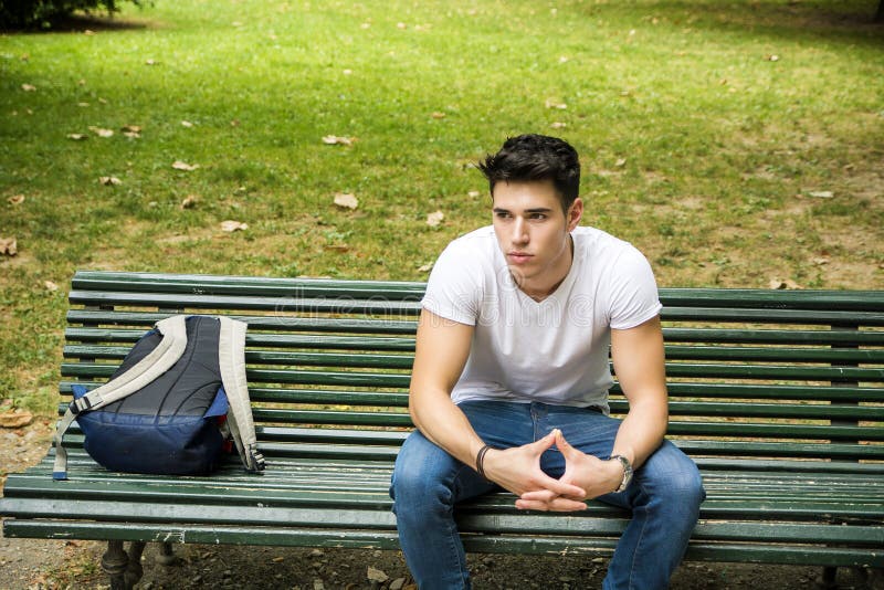 Estudiante masculino joven Sitting en banco de parque seriamente imágenes de archivo libres de regalías Estudiante masculino joven Sitting en banco de parque seriamente imágenes de archivo libres de regalías