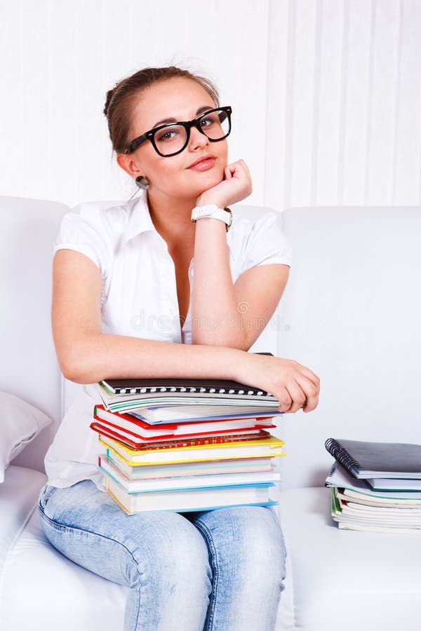 Smiling student in glasses sits on the sofa with books stack. Smiling student in glasses sits on the sofa with books stack