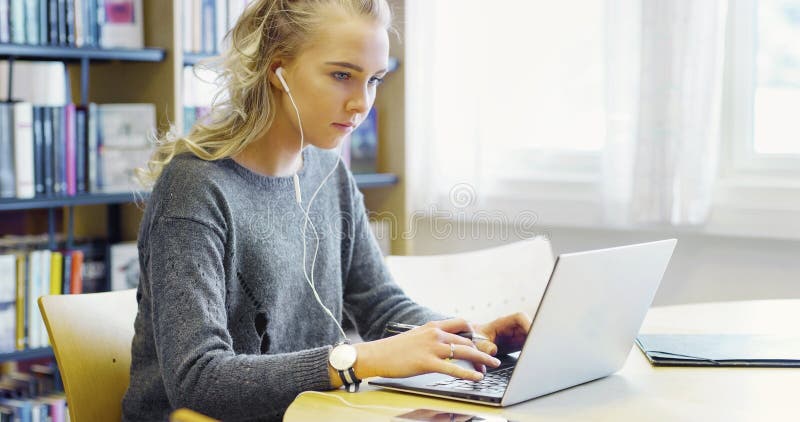 Estudiante trabajador que trabaja en el ordenador portátil en la biblioteca imagen de archivo Estudiante trabajador que trabaja en el ordenador portátil en la biblioteca imagen de archivo