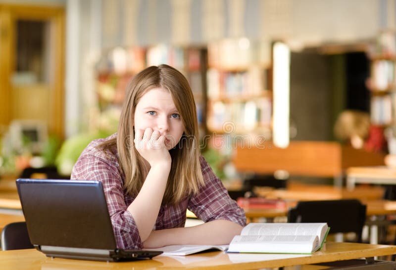 Estudiante triste con el ordenador portátil que trabaja en biblioteca imagen de archivo Estudiante triste con el ordenador portátil que trabaja en biblioteca imagen de archivo