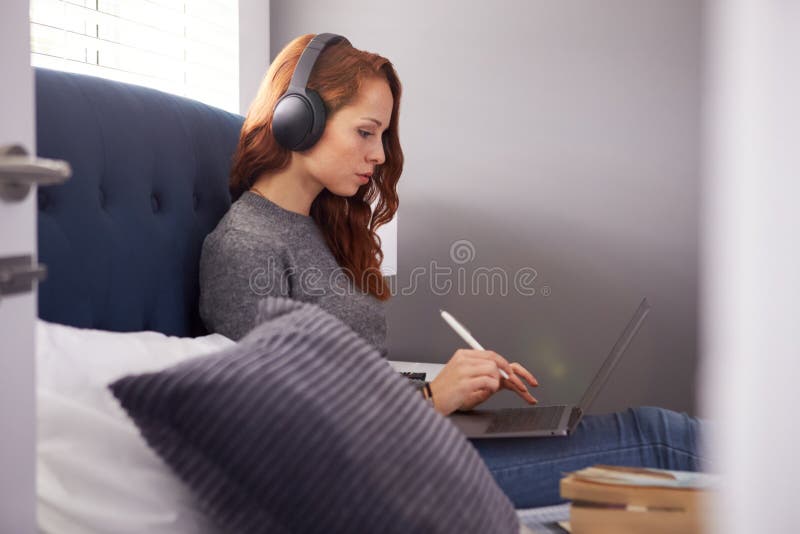 Estudiante Universitaria Viste Auriculares Inalámbricos Sentada En La Cama En Casa Compartida Usando Portátil