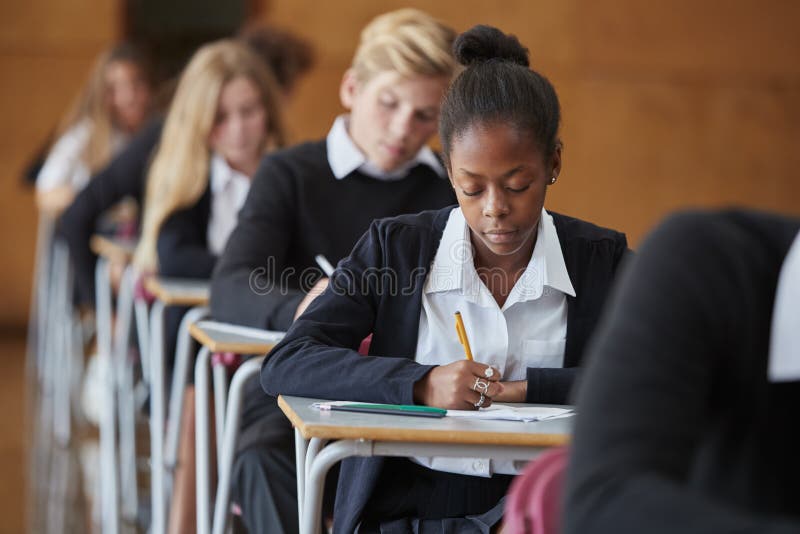 Estudiantes adolescentes en el examen que se sienta del uniforme en la escuela Pasillo foto de archivo Estudiantes adolescentes en el examen que se sienta del uniforme en la escuela Pasillo foto de archivo