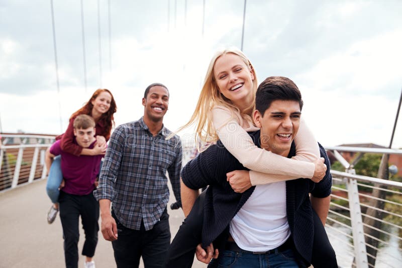 Estudiantes amigos y hombres que dan a las mujeres paseos por el Puente de la Ciudad imagenes de archivo