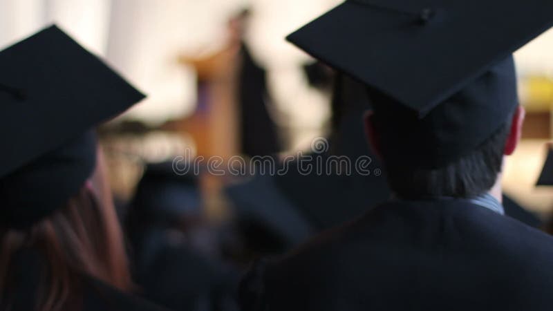 Estudiantes emocionados en casquillos y vestidos que aplauden en la ceremonia de graduación de la universidad