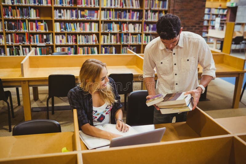 Estudiantes sonrientes que trabajan junto mientras que se sienta en la tabla imagen de archivo Estudiantes sonrientes que trabajan junto mientras que se sienta en la tabla imagen de archivo