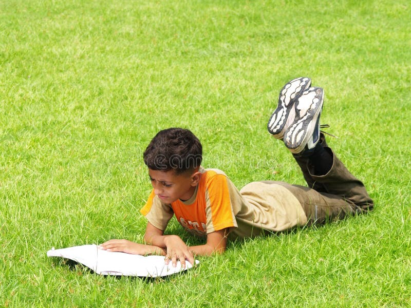 A young Asian boy lying on the grass, reading a book. A young Asian boy lying on the grass, reading a book.