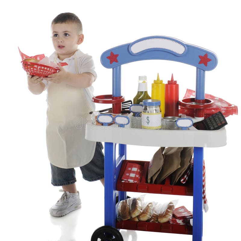 An adorable preschooler passing out a basket of hot dog and chips from behind his vendor stand. The stand's signs are left blank for your text. On a white background. An adorable preschooler passing out a basket of hot dog and chips from behind his vendor stand. The stand's signs are left blank for your text. On a white background.