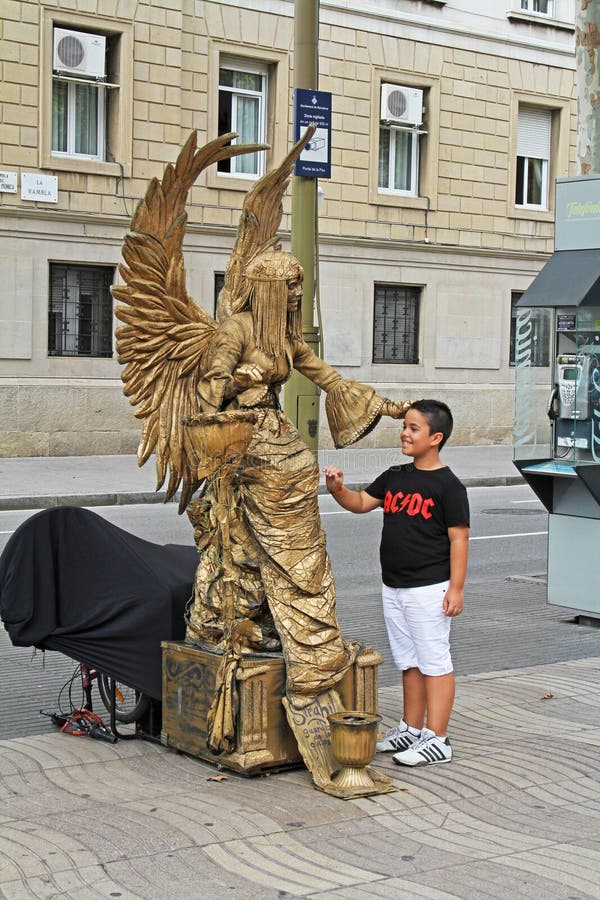 Estátua viva pintada dourada com asas e o menino de sorriso na rua de Ramblas em Barcelona fotografia de stock Estátua viva pintada dourada com asas e o menino de sorriso na rua de Ramblas em Barcelona fotografia de stock