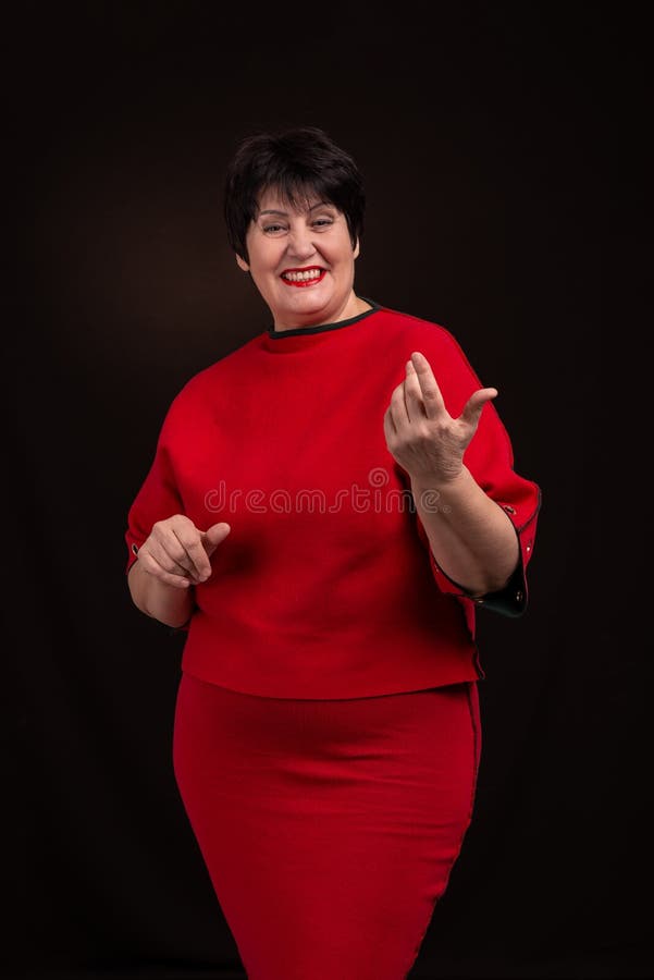 Estúdio disparado de uma mulher de sorriso adulta superior que veste um vestido vermelho em um fundo escuro Está sorrindo alegrem imagens de stock Estúdio disparado de uma mulher de sorriso adulta superior que veste um vestido vermelho em um fundo escuro Está sorrindo alegrem imagens de stock