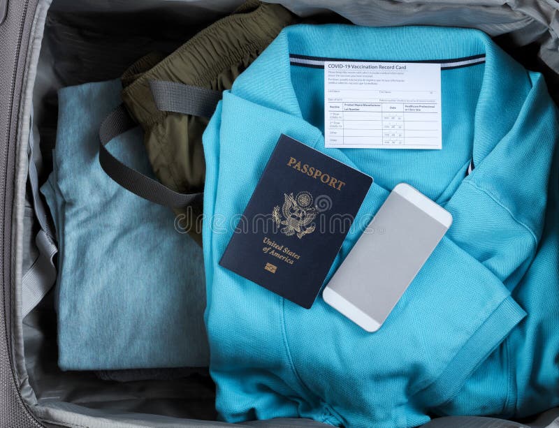 United States passport book with Covid 19 vaccination record card and smartphone inside of travel suitcase packed with clothes. United States passport book with Covid 19 vaccination record card and smartphone inside of travel suitcase packed with clothes